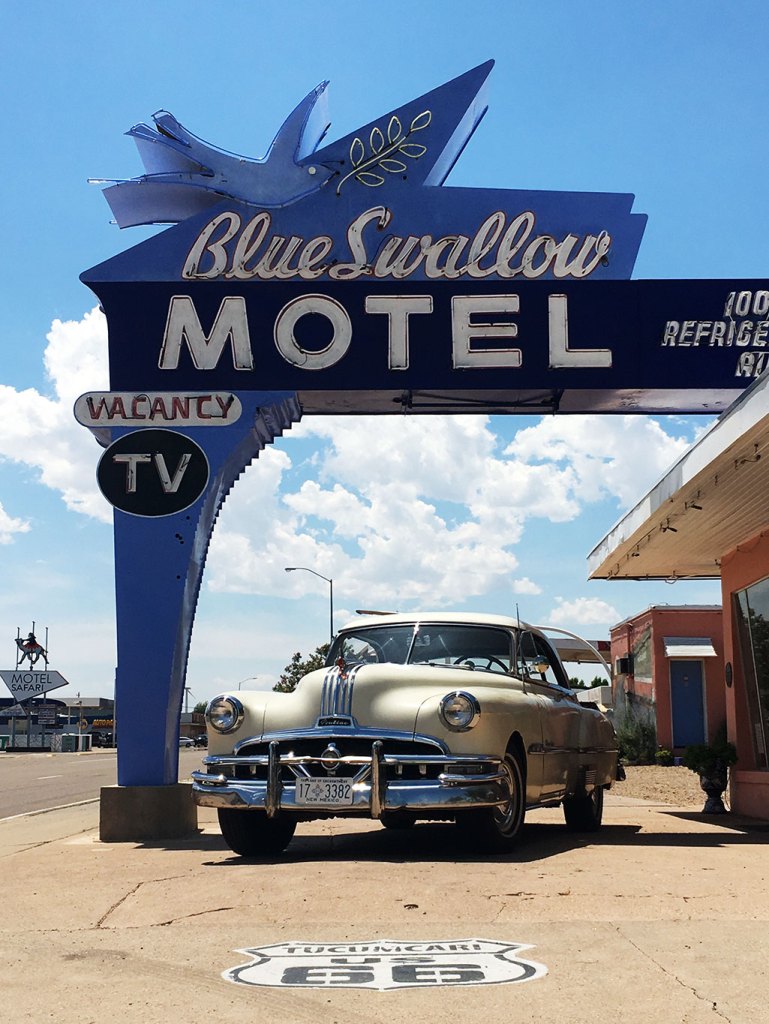 The recognizable classic Blue Swallow Motel sign in Tucumcari with a classic car parked beneath it.