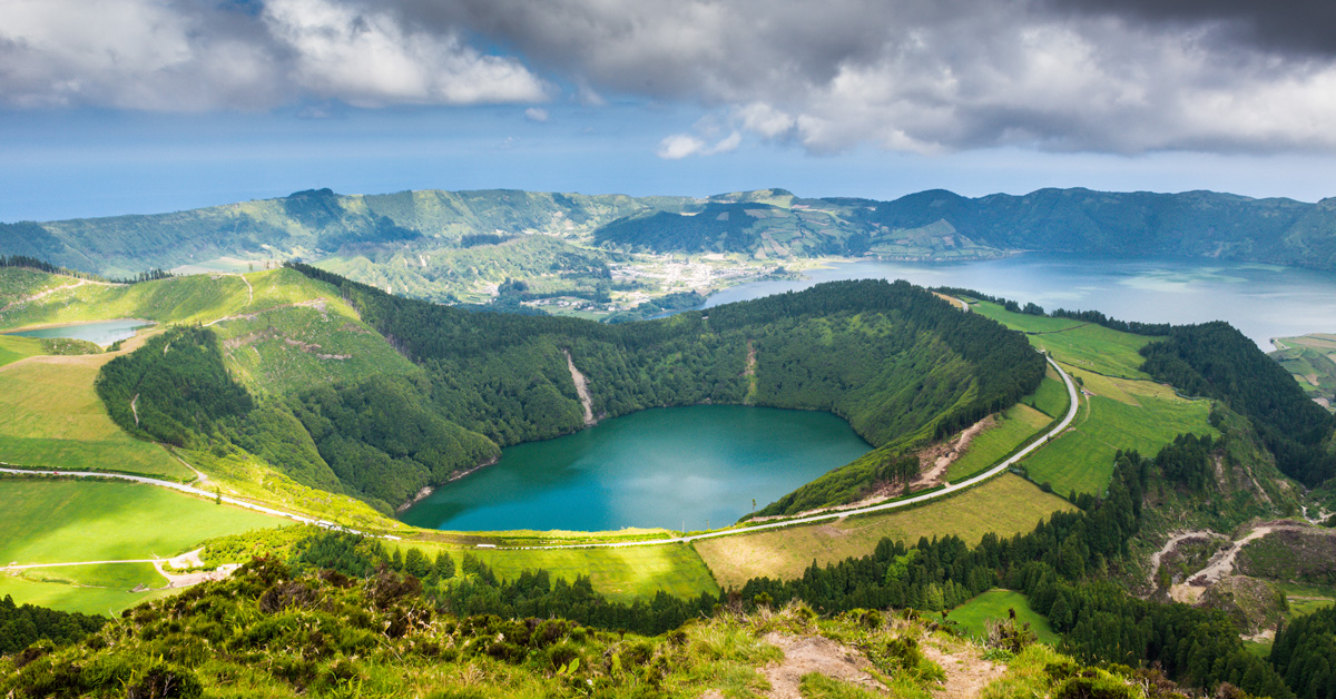 teal colored lake in a volcanic crater surrounded by green mountainous terrain