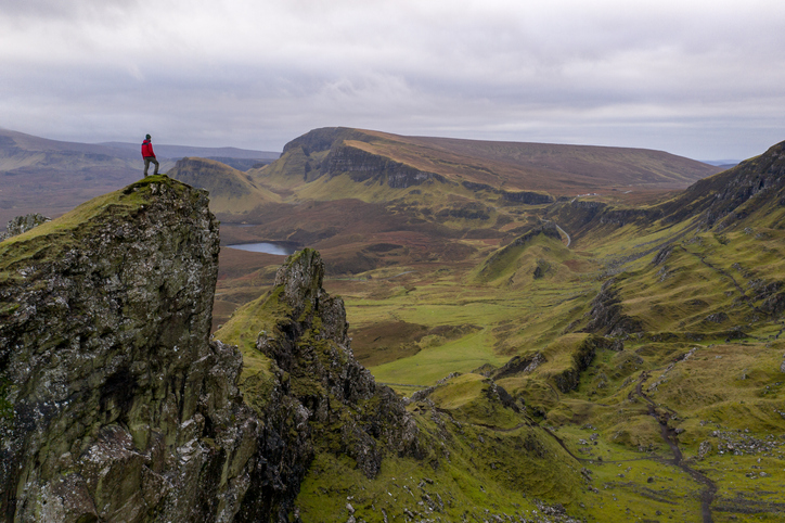 Hiker standing on mountain top in rugged volcanic landscape around Old Man of Storr, Isle of Skye, Scotland