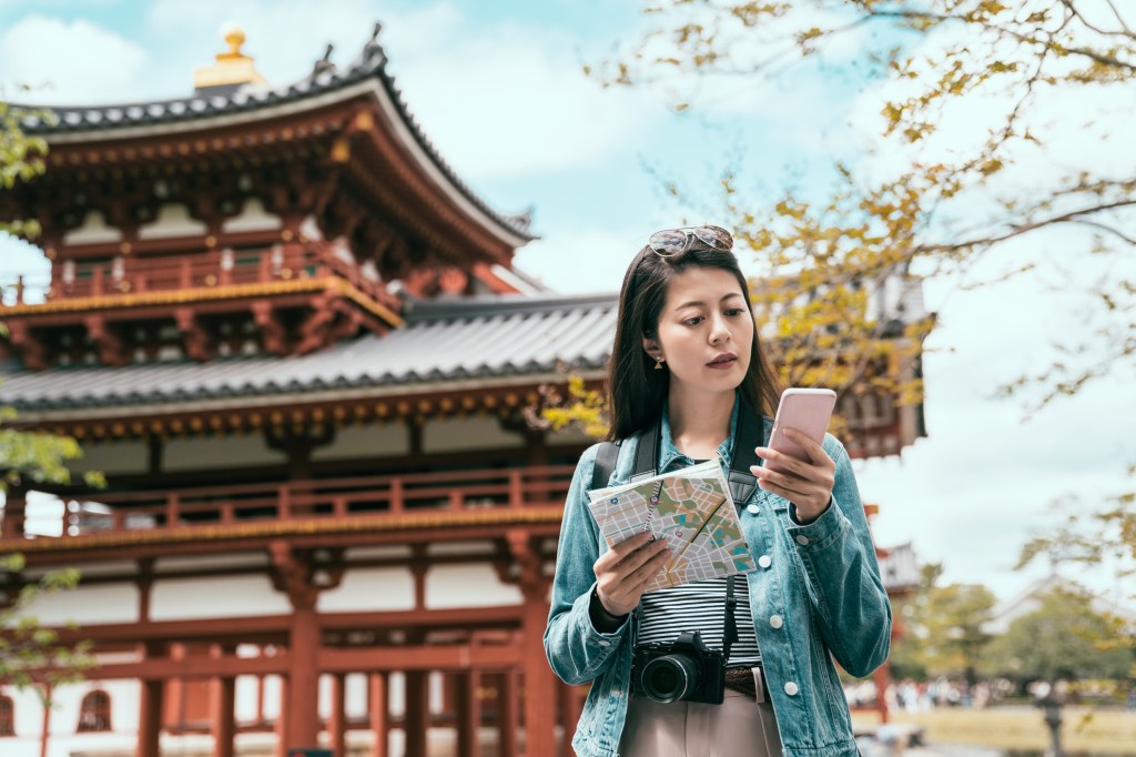 Woman in in front of a Japanese building holding a map and looking at her phone