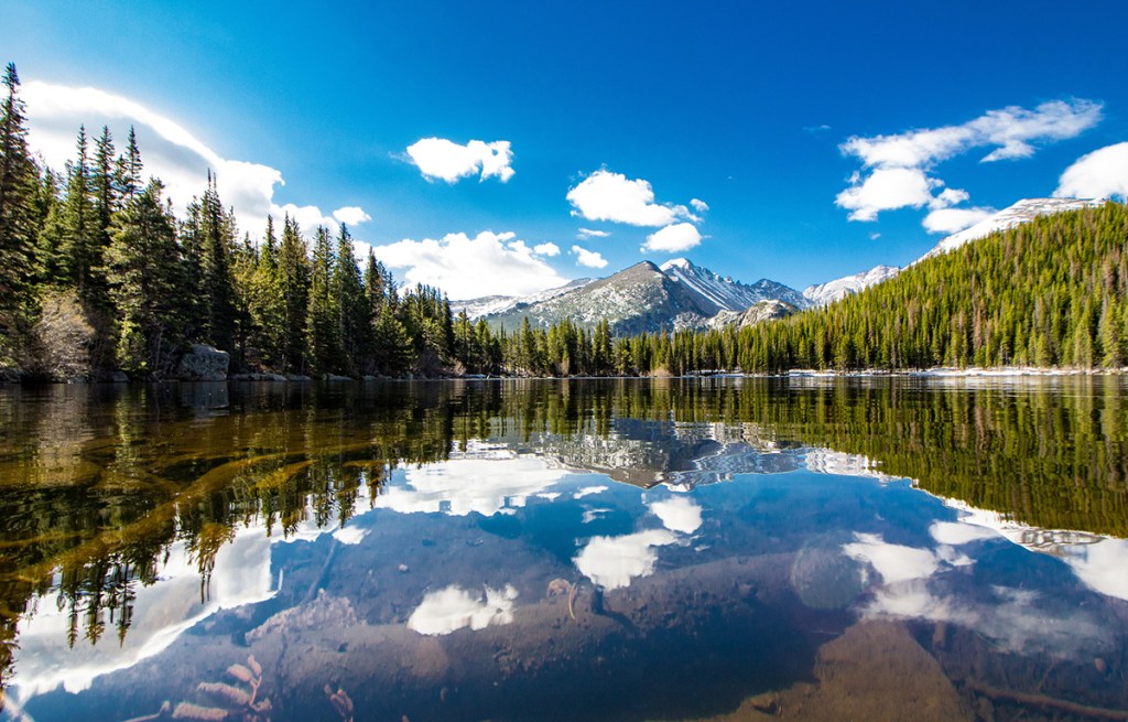 reflection of trees, mountain and clouds in a glassy lake surface