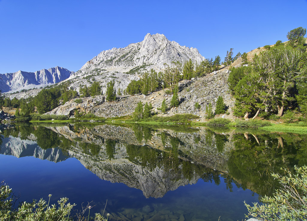 Photo of Long Lake and Bishop Pass with mountains, trees, and clear blue water