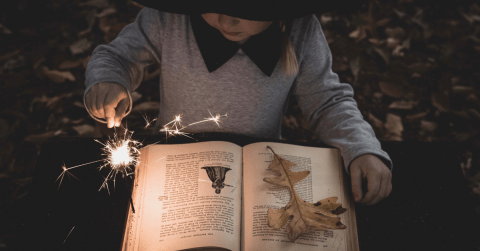 child in witch costume reading a book