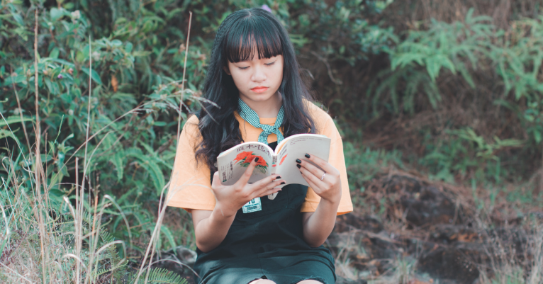 person reading a book outdoors surrounded by plants