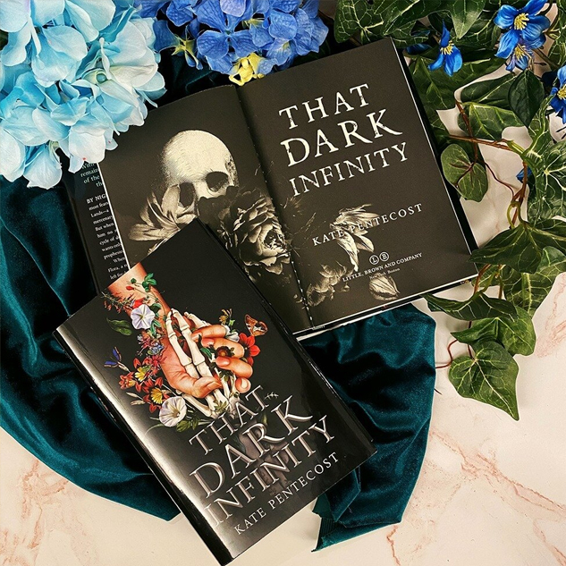 NOVL - Instagram image of book cover for 'That Dark Infinity' by Kate Pentecost, resting on top of a dark teal velvet cloth and surrounded by ivy and hydrangeas
