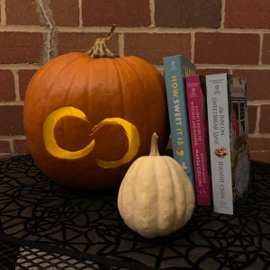 Pumpkin carved with Forever logo with 3 books leaning against it.