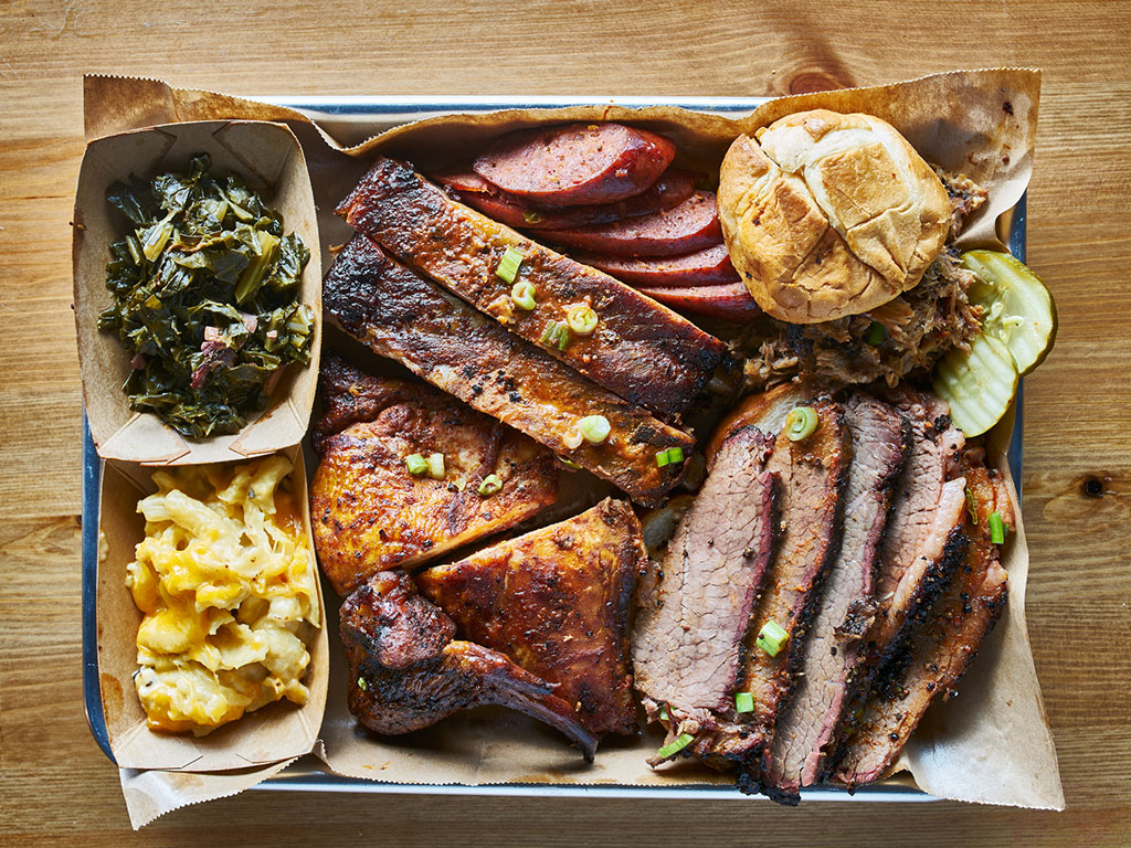 tray with various barbecued meats, greens, and mac and cheese in the texas style