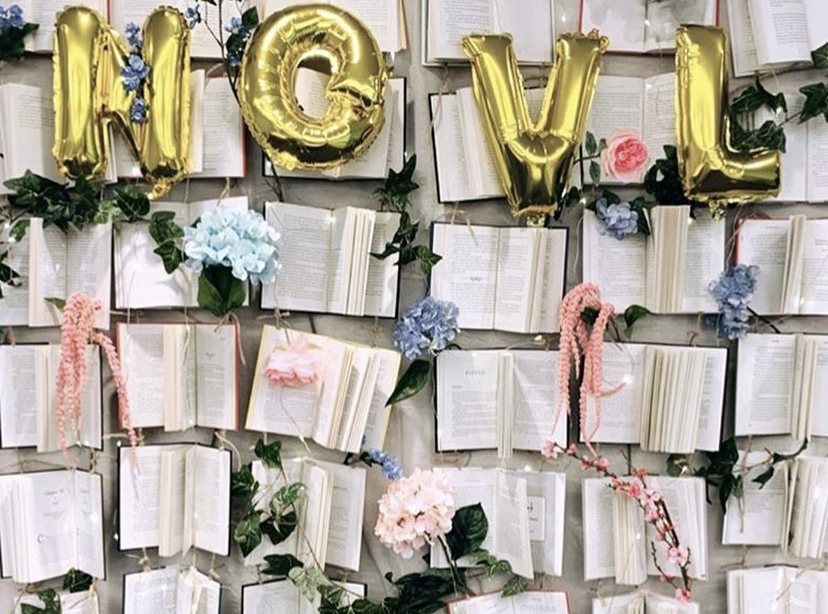 NOVL - Gold foil ballooonsin front of open books and flowers that reads 'NOVL'