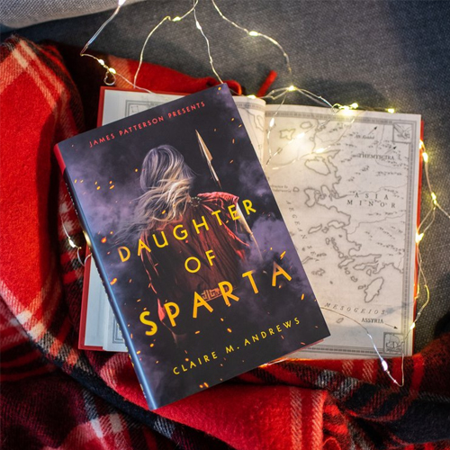 NOVL - Instagram image of 'Daughter of Sparta' by Claire M. Andrews resting on a blanket, surrounded by twinkle lights