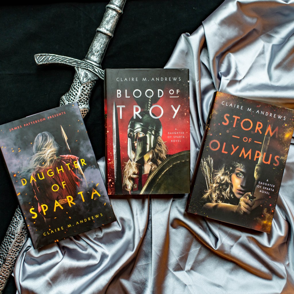 Image of the books "Daughter of Sparta", "Blood of Troy", and "Storm of Olympus" by Claire M. Andrews