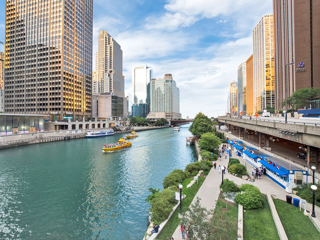 walkway alongside the chicago river with highrise buildings all around and blue sky ablove