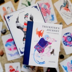 Photo of the Trickster's Journey keepsake box and included guidebook laid atop face-up cards from the deck.