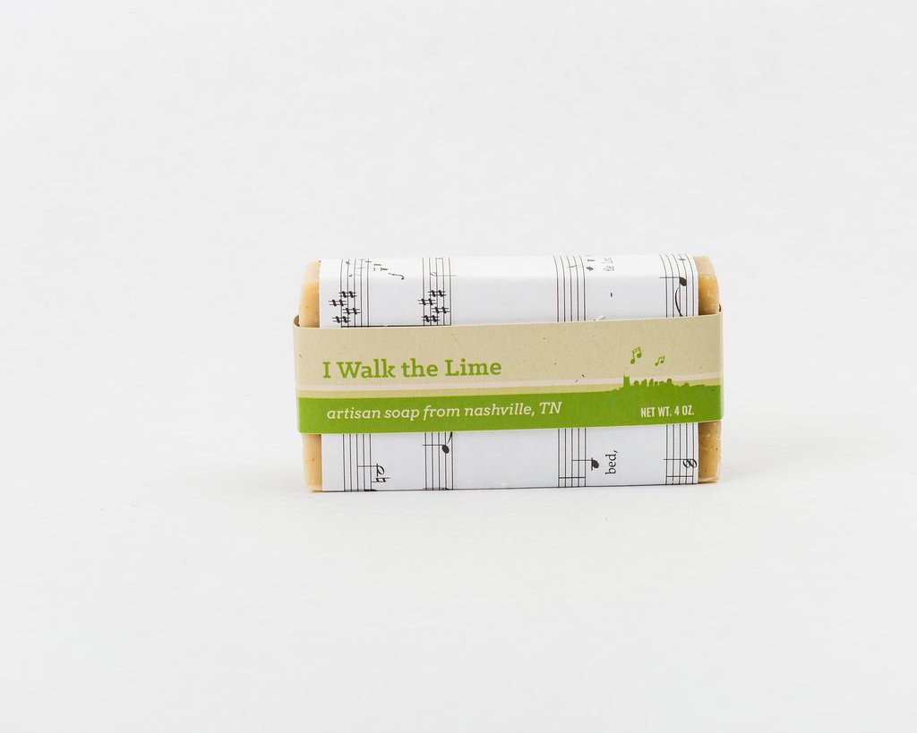 A bar of soap wrapped in sheet music and a green paper band printed with text "I Walk the Lime. Artisan soap from Nashville TN" 