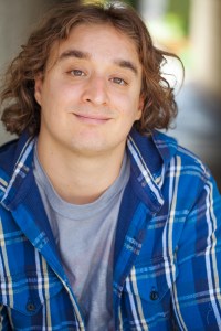 Headshot image of illustrator Jake Tashjian, smiling while wearing a plaid blue button down