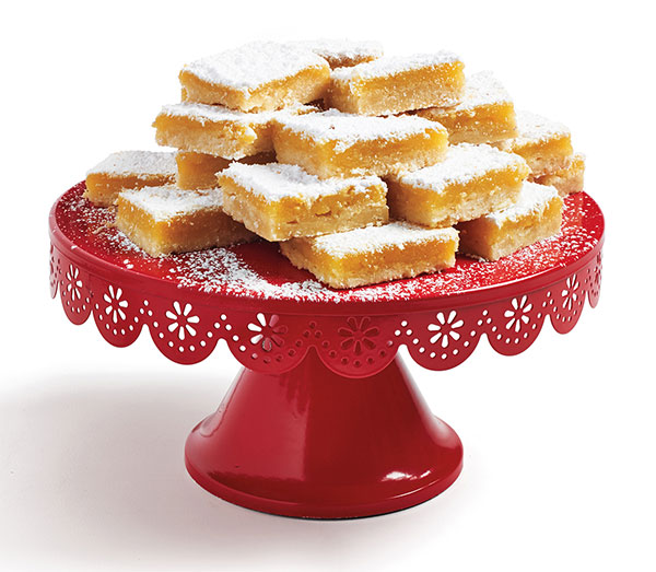 Photo of lemon squares stacked on top of a red cake stand.