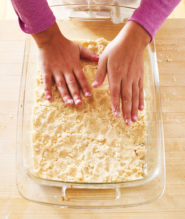 Photo of hands pressing dough into the baking pan to form a flat layer.