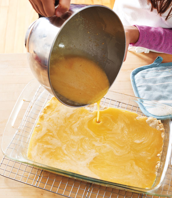 Photo of hands pouring lemon mixture on top of the crust.