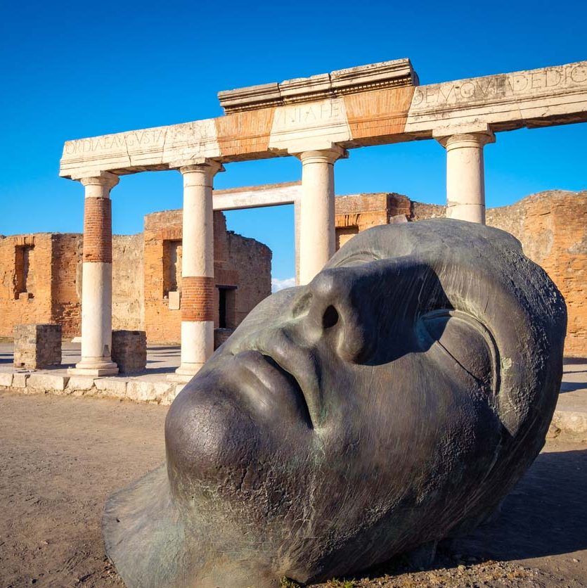 Ruins and a large bronze head in ancient Pompeii city, Italy.