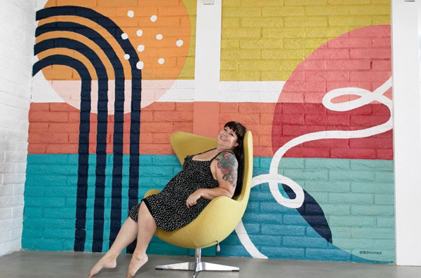 Photo of person sitting in front of a geometric mural.