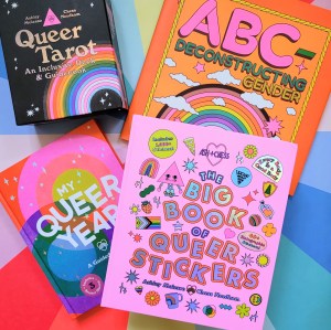 Photo of Ash + Chess' collected titles laid above a colorful ranbow burst backdrop. From top left clockwise: "Queer Tarot," "ABC-Deconstructing Gender," "The Big Book of Queer Stickers," and "My Queer Year"