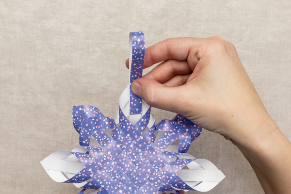 Photo of a hand holding a colored paper strip loop a the top of the star to create a hanger.