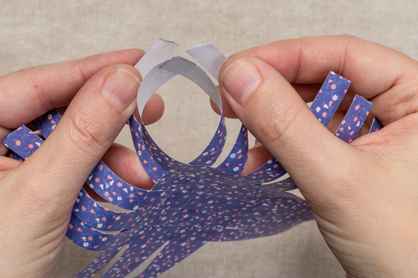 Photo of someone folding the ends of a woven paper cross together.