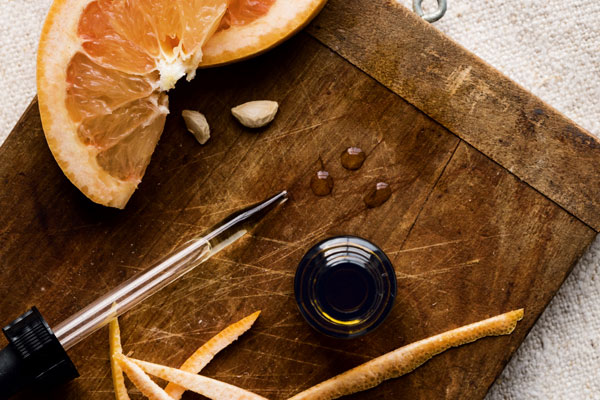 Photo of an oil dropper on a wooden platter with slices of orange and orange peel.