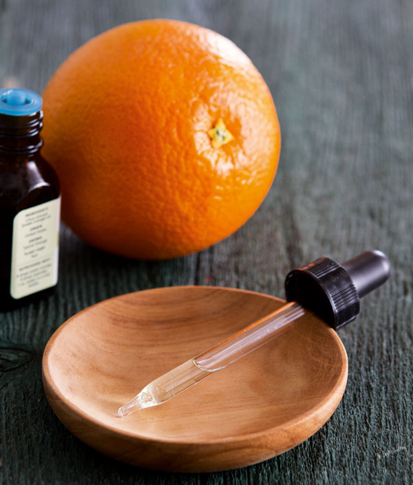 Photo of a liquid dropper in a small wooden bowl, with a small glass bottle and orange in the background.