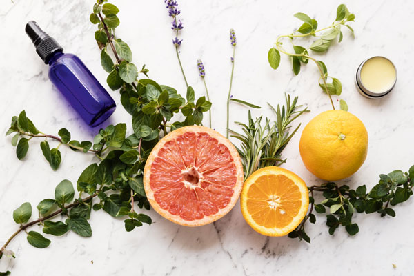 Photo of citrus fruits, grapefruit, orange, and lemon, on a spread of herbs with a small blue spray bottle and tin of balm.