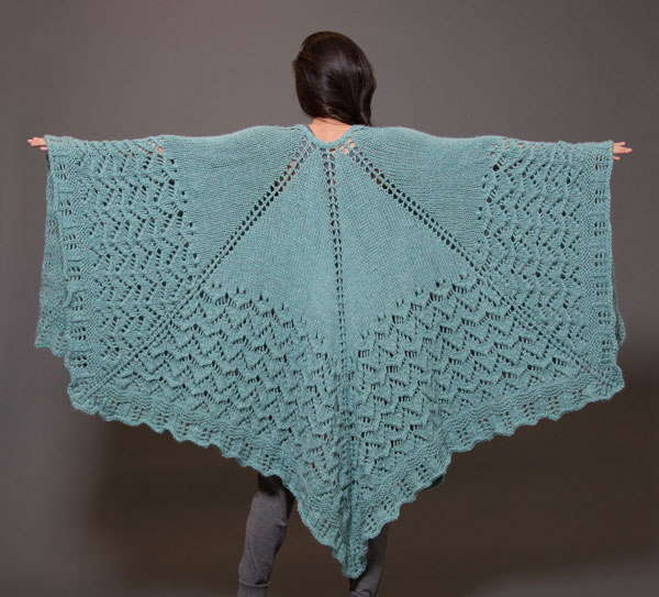 Photo of the back of a woman wearing a shawl with her arms extended.