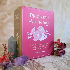 Photo of "Pleasure Alchemy" standing among flowers and crystals, against a gold marble background