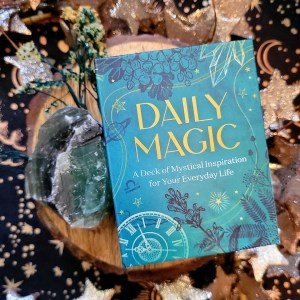 Photo of "Daily Magic" laid on a short decorative log with a crystal and flowers