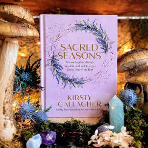Photo of "Sacred Seasons" in a nature setting, surrounded by crystals and mushrooms