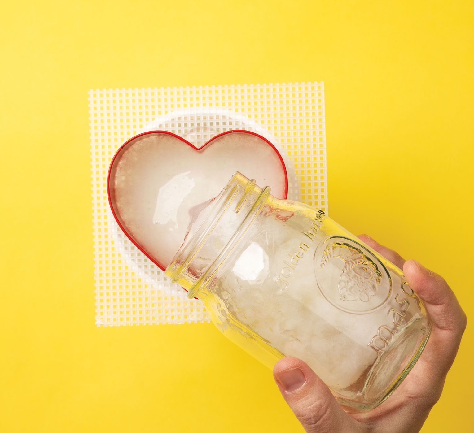 Photo of paper and water mixture being poured into a heart-shaped cookie cutter over a mesh screen.