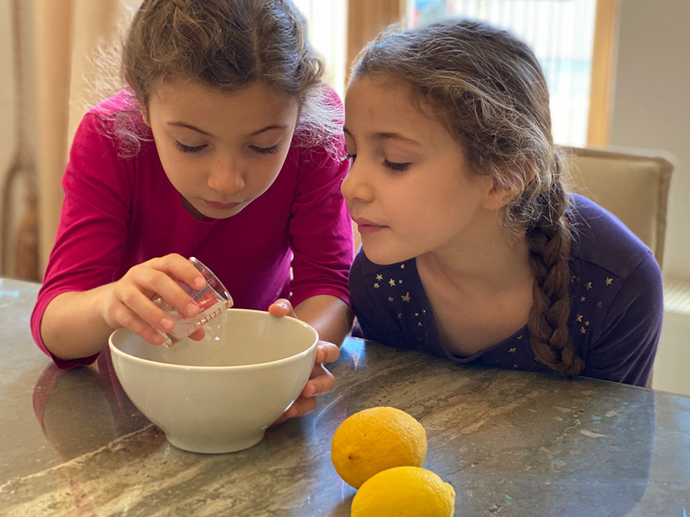 Photo of two young girls pouring lemon juice from a measuring cup into a bowl.