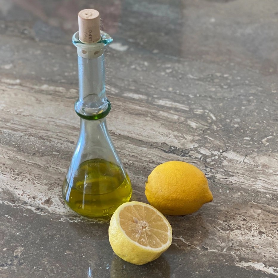 Photo of a glass containing oil and a whole lemon, and half lemon, on a granite countertop.