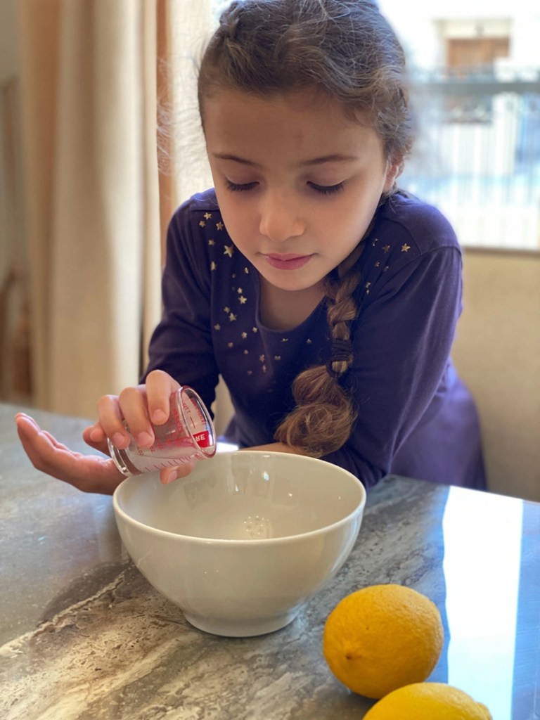 Photo of a young girl pouring lemon juice from a measuring cup into a white bowl.