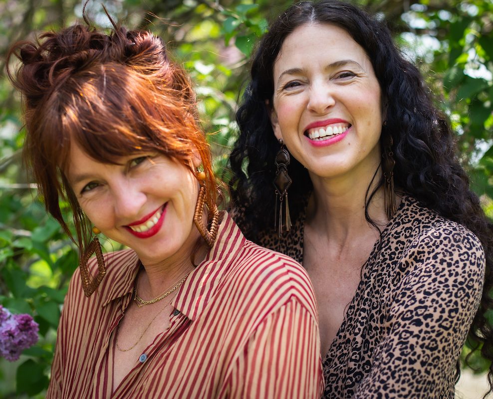 Photo of author Anne Louise Burdett and illustrator Chelsea Granger hugging each other and smiling joyfully at the camera in front of greenery and flowers