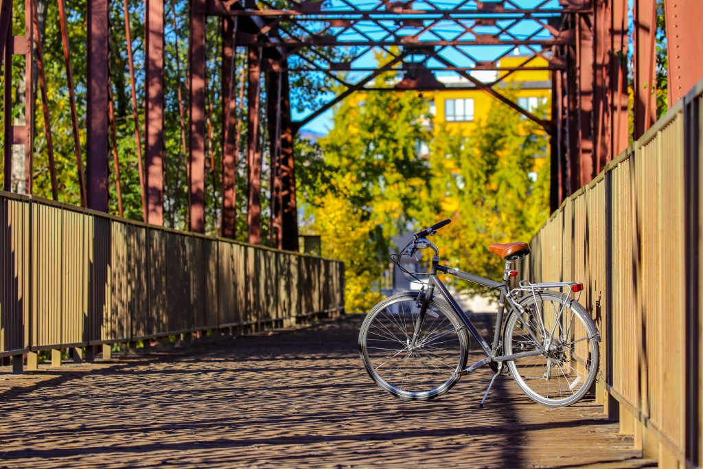 A bike parked on a charming rust-colored bridge with yellow-green trees in the background.