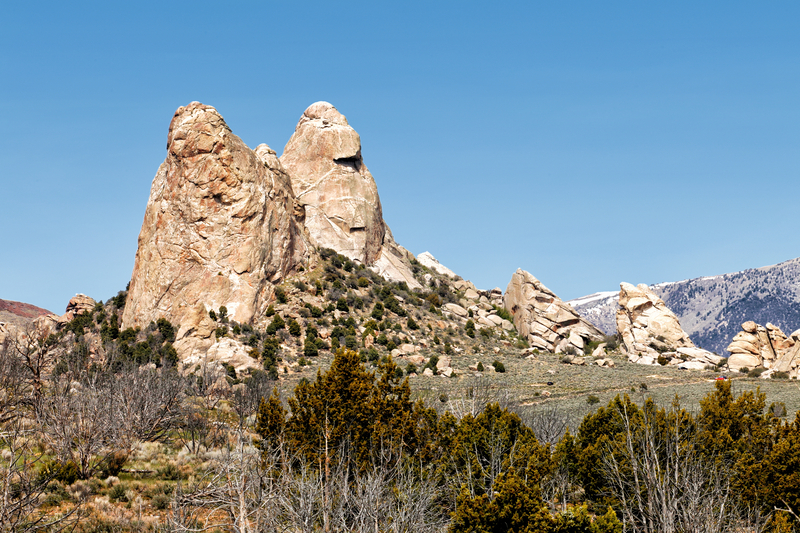 Sandy-colored rock formations rise up from desert hills covered in scrub brush.