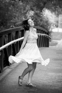 Black and white photo of author Nikki Van De Car laughing in mid-twirl while wearing a summery dress