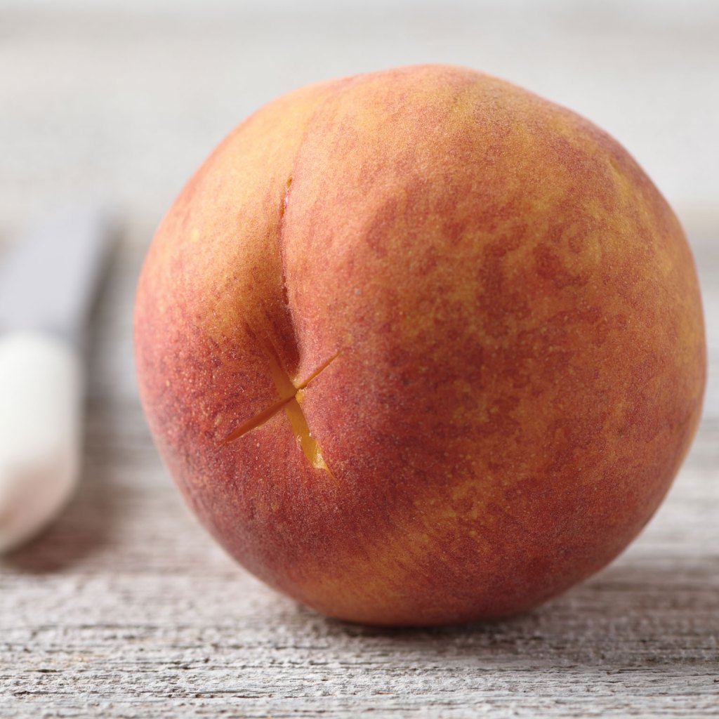 A photo of the bottom of a peach with a small X cut into the skin.