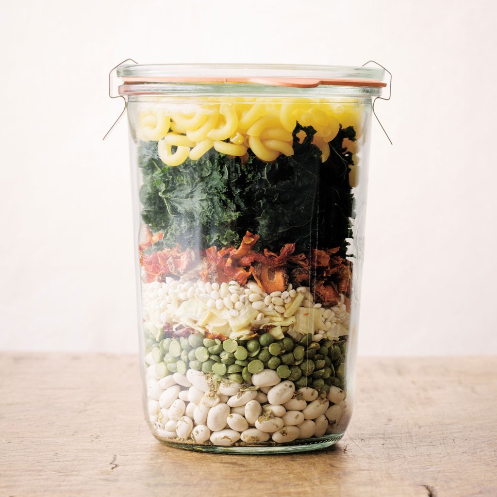 Photo of glass jar layered with dried beans, dried vegetables, and dried pasta.