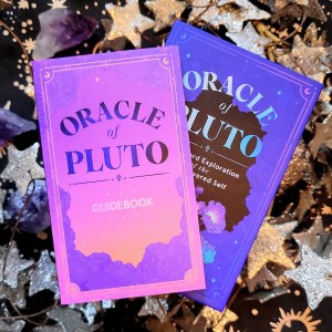 Photo of the Oracle of Pluto deck box and guidebook above a starry background