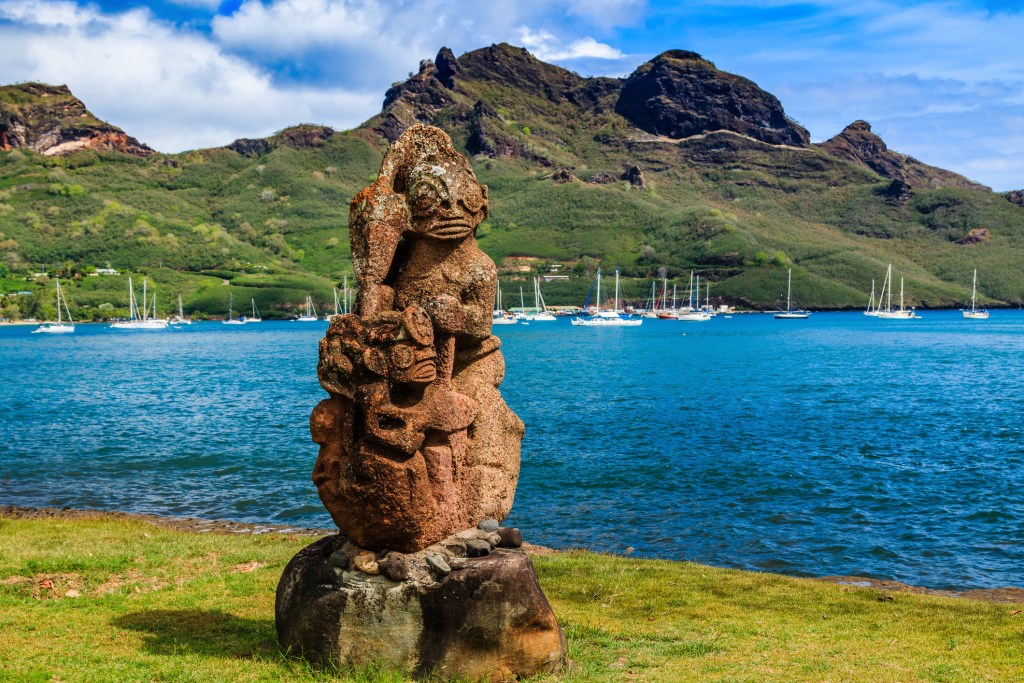 An ancient stone sculpture perched on land at the edge of an ocean bay.