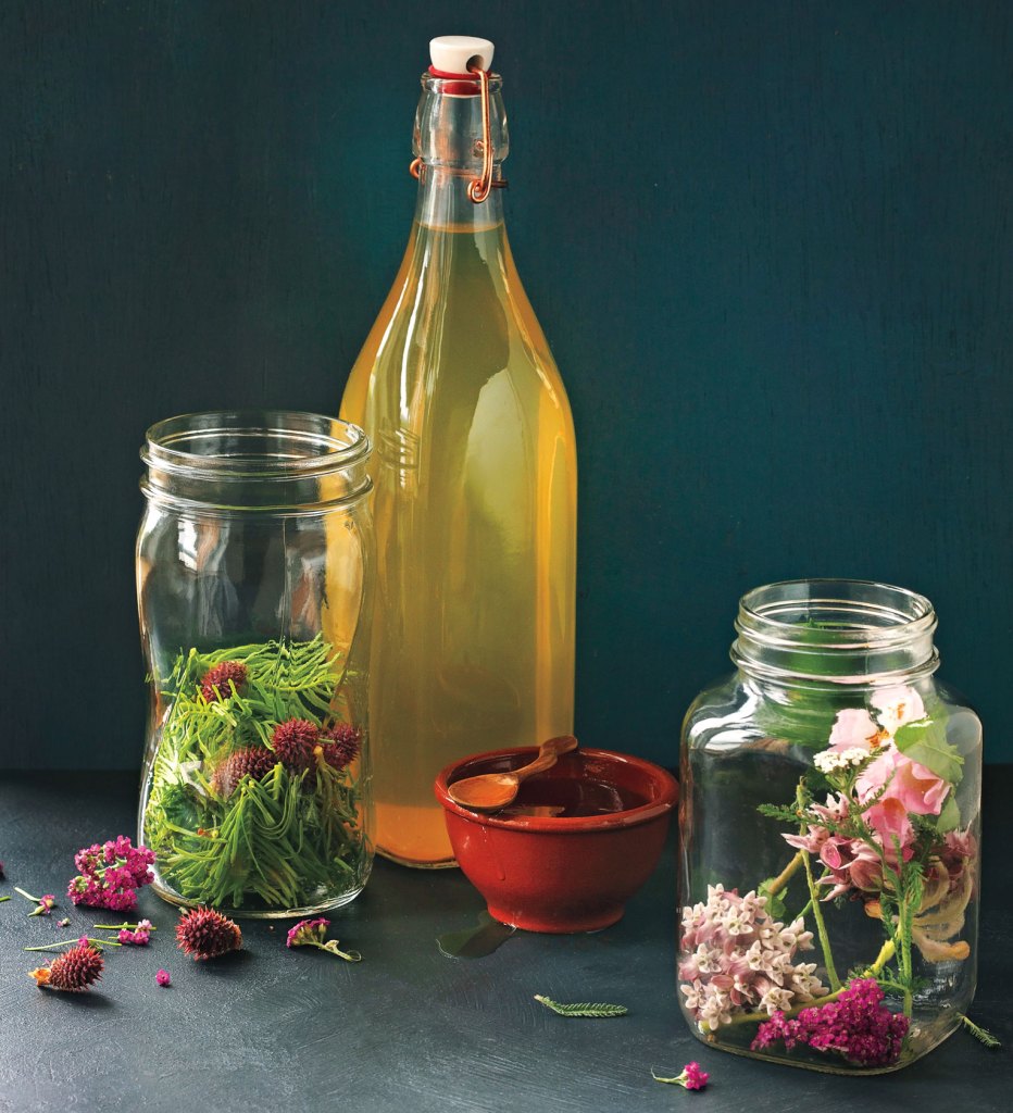 Photo of bottle of vinegar with jars filled with flowers and herbs.