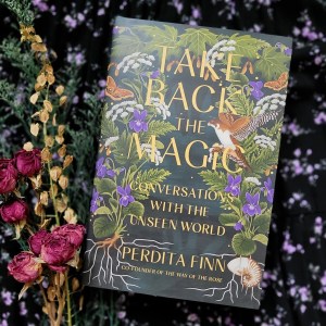 Photo of "Take Back the Magic" laid next to a boudquet of flowers against a dark floral background
