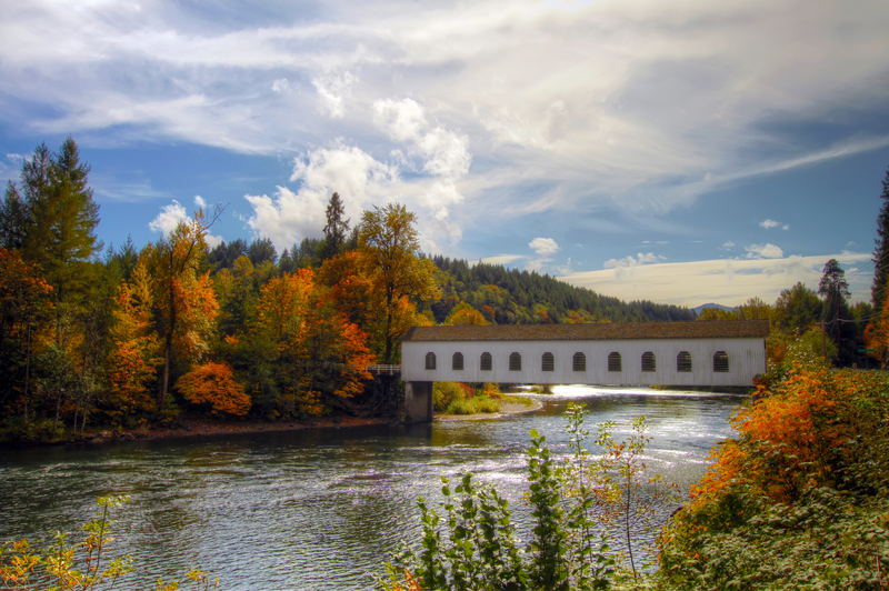 white, wooden covered bridge stretching across a calm river in the fall