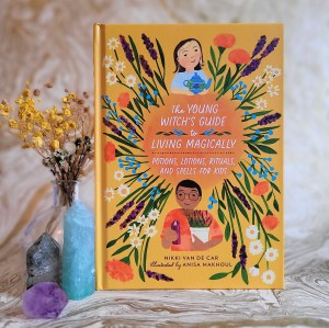 Photo of "The Young Witch's Guide to Living Magically" standing next to yellow flowers and two large crystals, against a marbled background