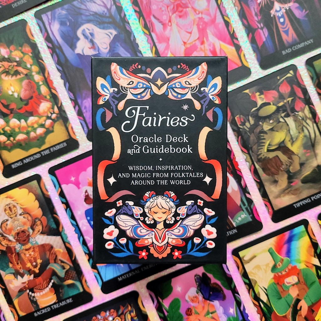 Photo of the "Fairies Oracle Deck and Guidebook" box laid atop face-up cards from the deck